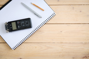 Digital sound recorder and other accessories on the wooden table, top view
