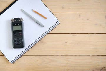 Digital sound recorder and other accessories on the wooden table, top view