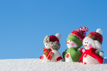 The winter, Christmas - three happy snowmen stand against the background of the blue sky.