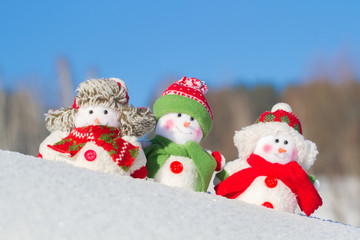 The winter, Christmas - three happy snowmen stand against the background of the blue sky.