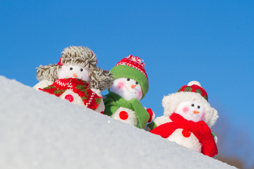 The winter, Christmas - three happy snowmen stand against the background of the blue sky.