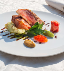 Grilled tuna with mashed potatoes, wasabi, miso aioli, red caviar and marinated ginger. On white plate and restaurant table.