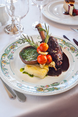 Stewed leg of lamb with portobello mushroom, potato gratin, rosemary, tomatoes and red wine sauce. On white tablecloth and wine glasses on background.