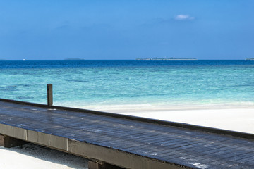 Fototapeta na wymiar Black wooden pontoon heading in to the indian ocean located on a white sand beach somewhere on maldives.