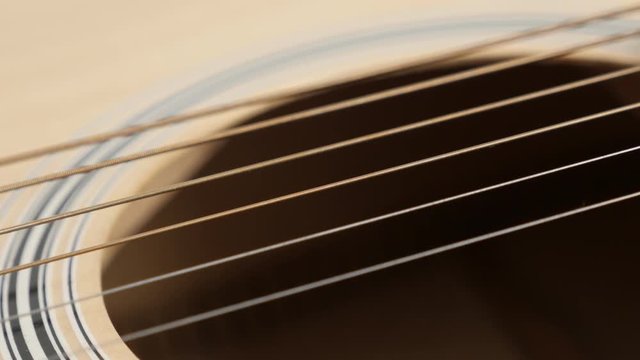 Close-up of wooden acoustic guitar strings shallow DOF 4K 2160p 30fps UltraHD panning footage - Details of plucked string instrument body slow pan 3840X2160 UHD video