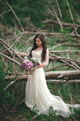 Beautiful bride in the forest with a large bouquet of different flowers. Rustic style