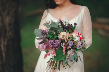 Beautiful bride in the forest with a large bouquet of different flowers. Boho style