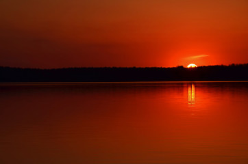 Sunset over the forest lake in red tones