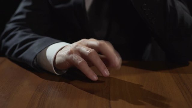 Frustrated mafia boss drumming fingers on table, thinking or making decision