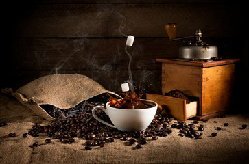 coffee art composition: scattered roasted beans from a bag, coffee grinder with ground coffee and a...