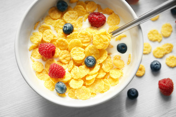 Tasty cornflakes with raspberries and blueberries on table