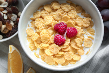 Tasty cornflakes with raspberries on table