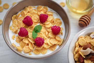 Tasty cornflakes with raspberries and honey on table