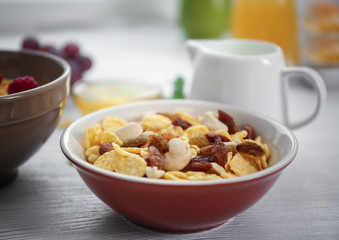 Tasty cornflakes with raisins and nuts and honey on table