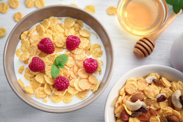 Tasty cornflakes with raspberries and honey on table
