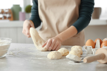 Woman making small balls of dough on table in kitchen