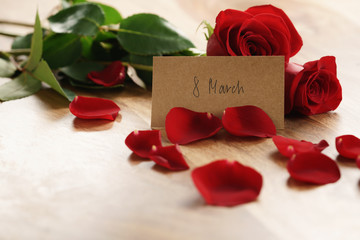 three red roses and petals on old wood table with 8 march paper card, romantic background