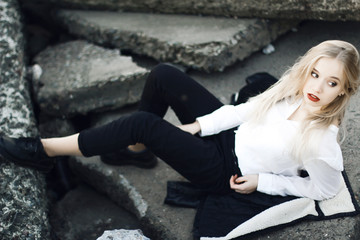 blonde girl with wavy long hair sitting on the rocks. chenye her wearing pants and a white shirt. she look away