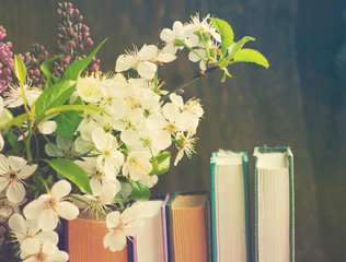 Pile of books and spring flowers of a lilac and apricot on a wooden background. 