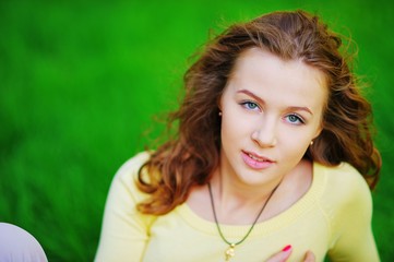 Portrait of a young pretty girl with brown hair with a calm expression, sitting on a green lawn in a Park on a clear Sunny day, close-up