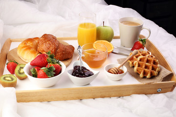 breakfast in bed with fruits and pastries on a tray -waffles, croissant