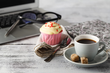 Coffee cup and muffin on table with computer