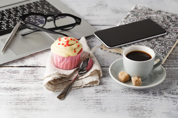 Coffee cup and muffin on table with computer