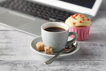 Coffee cup and muffin on table with computer