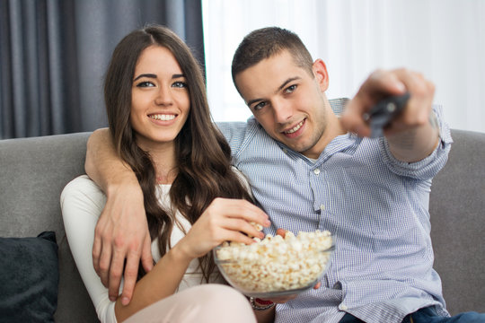 Young couple watching tv and eating popcorn at home
