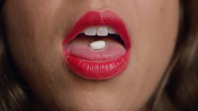 Woman in red lipstick sticks out her tongue to reveal a white pill. Swallows it.