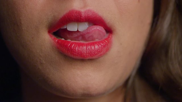 Woman in red lipstick runs her tongue over her teeth, suggestively.