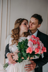 cute wedding couple in the interior of a classic white studio decorated. hey kiss and hug each other, holding hands looking at each other