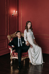 cute wedding couple in the interior of a classic studio with red background . hey kiss and hug each other, holding hands looking at each other