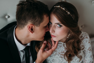 cute wedding couple in the interior of a classic white studio decorated. hey kiss and hug each other, holding hands looking at each other