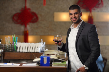 Handsome young man is standing at the bar and holding a glass of red wine.