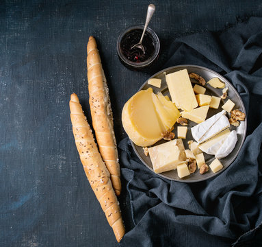 Cheese plate. Assortment variety of cheese with walnuts, jam and bread on vintage metal plate with textile over dark blue canvas as background. Top view with space. Appetizer theme
