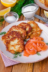 Potato pancakes with sour cream and salmon on a plate on a wooden background