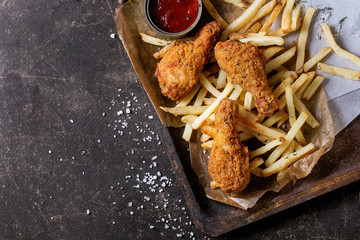 Fast food fried crispy chicken legs and french fries potatoes with salt and ketchup sauce served on...