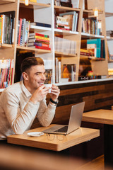 Cheerful young man sitting in cafe while drinking coffee.