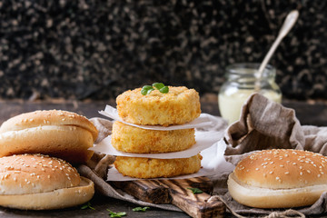 Ingredients for making vegan burger. Veggie cheese and onion cutlets, yogurt sauce, hamburger bunsand  herbs , served on wooden board with textile on dark background. Healthy vegan food.