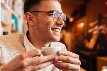 Cheerful young man sitting in cafe while drinking coffee