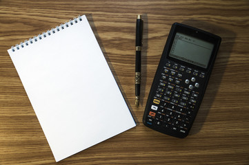 Notepad, fountain pen and calculator on wooden background