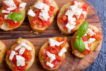 Bruschetta small sandwiches antipasto set with tomato, mozzarella, garlic and basil on black background