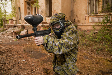 Fototapeta premium young boy playing paintball. boy aiming a paintball gun. Boy in camouflage clothing. boy in a protective suit. Boy in a protective mask. game of war. war game. Boy shoots a gun.