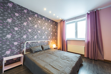 Fototapeta premium Interior bedroom with a large double bed with bedside tables, window on a background of modern wallpaper