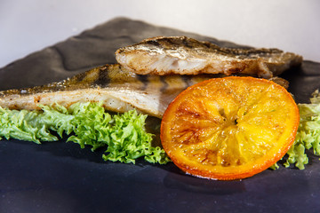 Fried fish (cod) with grilled orange lies on the plate.