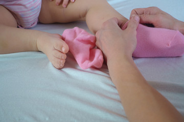 Mother puts pink socks on baby's legs in the bed