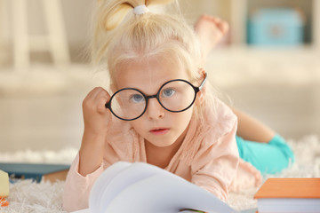 Small girl in glasses with many books on carpet