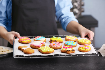 Woman holding baking grid with colourful Easter cookies, closeup