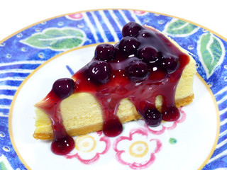 Piece of baked cheesecake with blueberry sauce served on vibrant colored pattern plate 